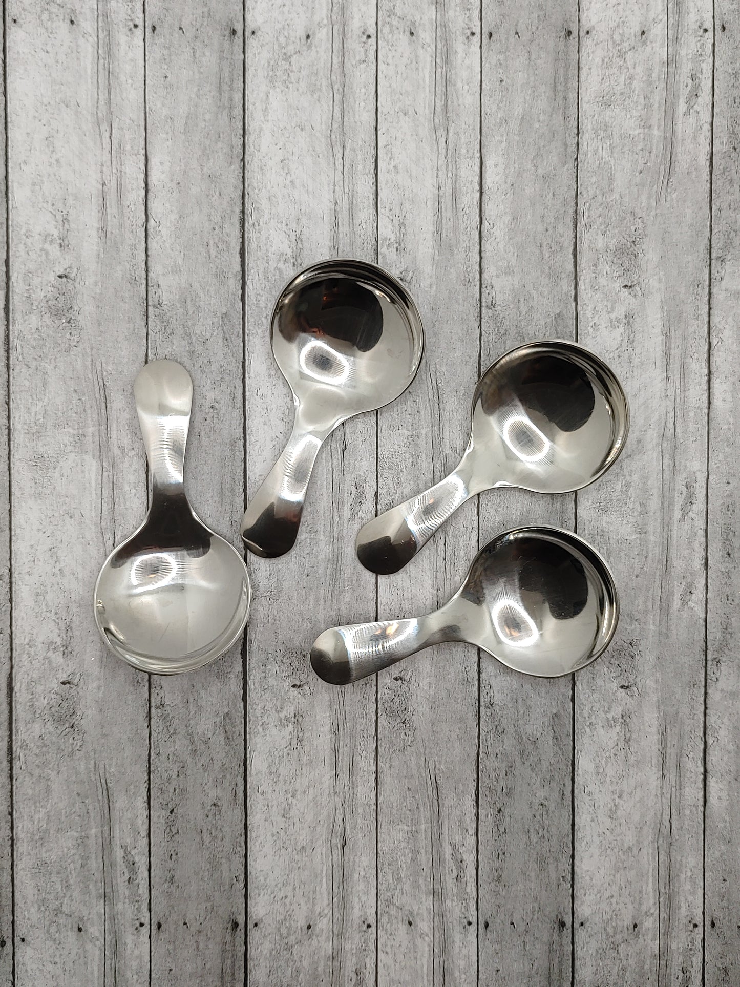 Four silver serving spoons with a solid pattern, displayed against a wooden background.