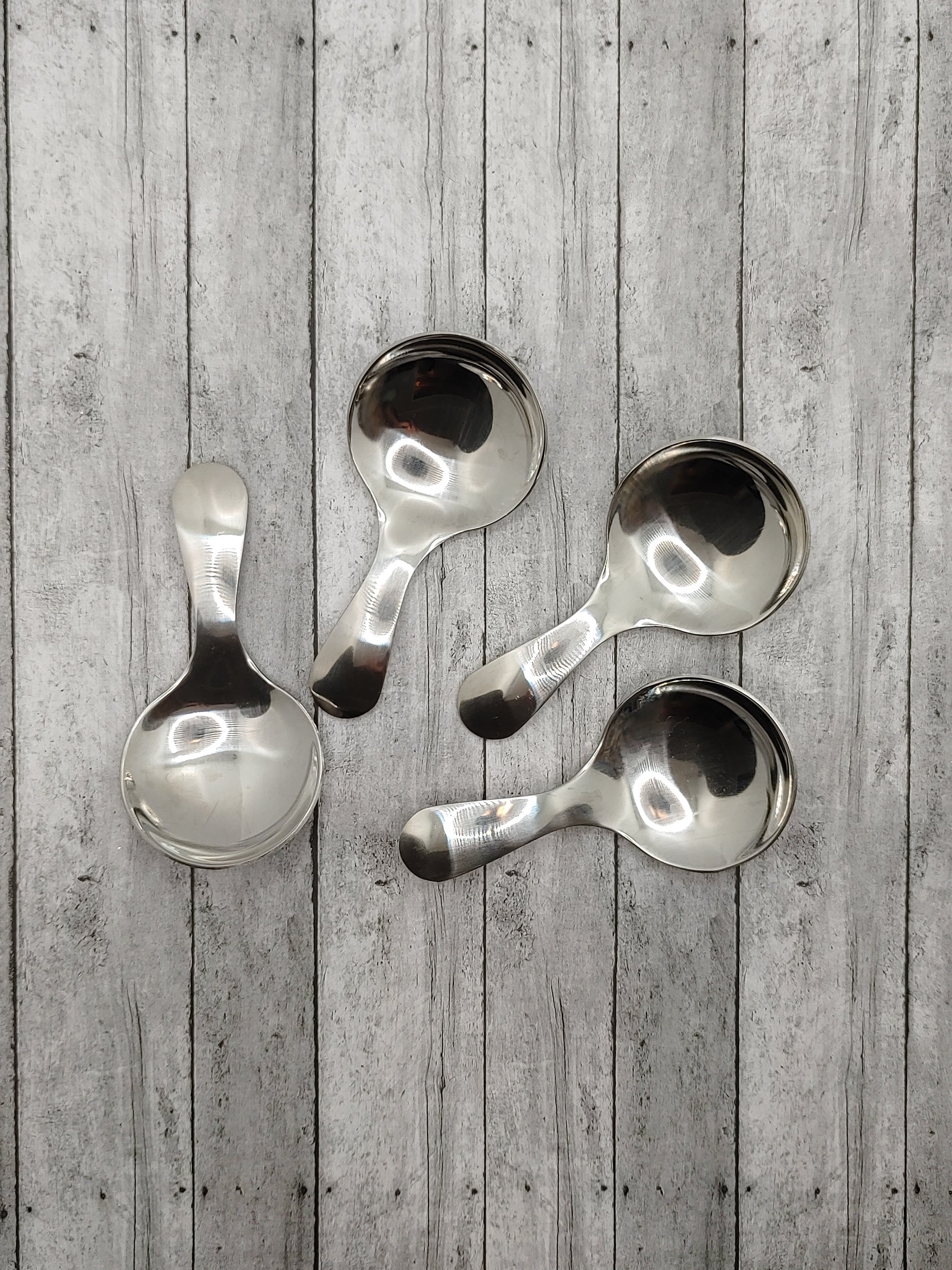 Four silver serving spoons with a solid pattern, displayed against a wooden background.